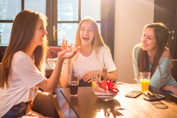 Szczęśliwe nastolatki rozmawiają i śmieją się w kawiarni. - Zdjęcie, obraz