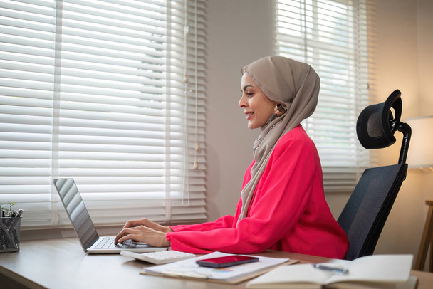 ヒジャブを着用している若いムスリム起業家は,プライベートオフィスで個人事業を管理するラップトップと協力しています.. - 写真・画像