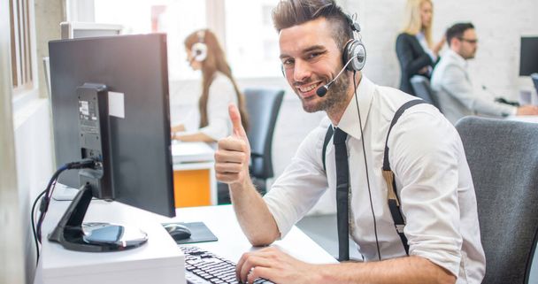 Vriendelijke online customer support agent met headset tonen duim omhoog in call center - Foto, afbeelding