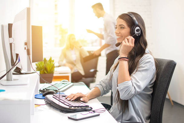 Mujer de negocios sonriente u operador de línea de ayuda con auriculares usando computadora en la oficina - Foto, Imagen