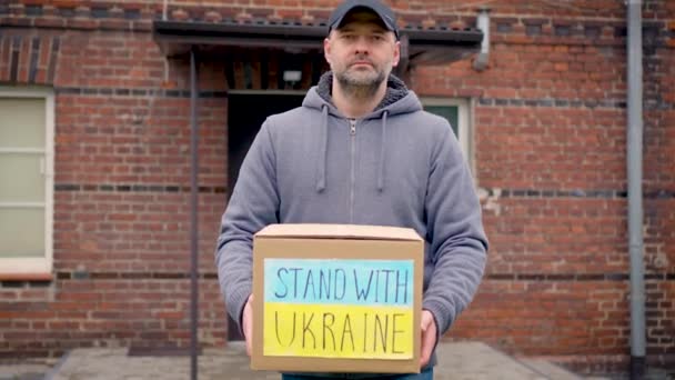 責任あるボランティアの男性は,雪の下で冬に手にウクライナ難民のための寄付された食糧と人道援助のボール紙を運びます. ロシア侵略との戦争でウクライナを助ける - 映像、動画