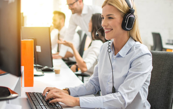Young female customer service executive in headset working on computer in call center - Photo, Image