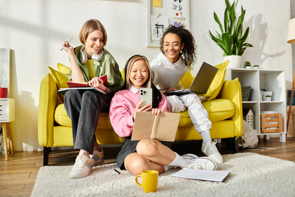 Trzy nastolatki różnych ras siedzą razem na żółtej kanapie. Wygląda na to, że uczą się i cieszą swoim towarzystwem.. - Zdjęcie, obraz