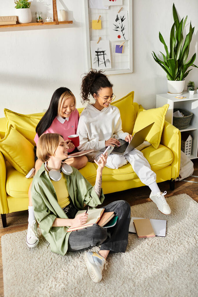 Un grupo diverso de chicas riendo mientras se sientan encima de un sofá amarillo brillante dentro de una habitación acogedora. - Foto, Imagen