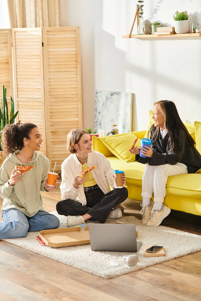 Группа разнообразных девочек-подростков, сидящих на полу, делящихся смехом и пиццей в уютном доме. - Фото, изображение