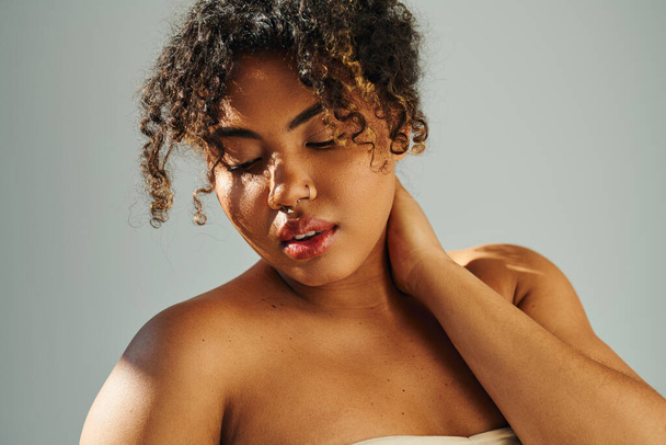Elegante Afro-Amerikaanse vrouw in strapless jurk masseren haar nek teder. - Foto, afbeelding