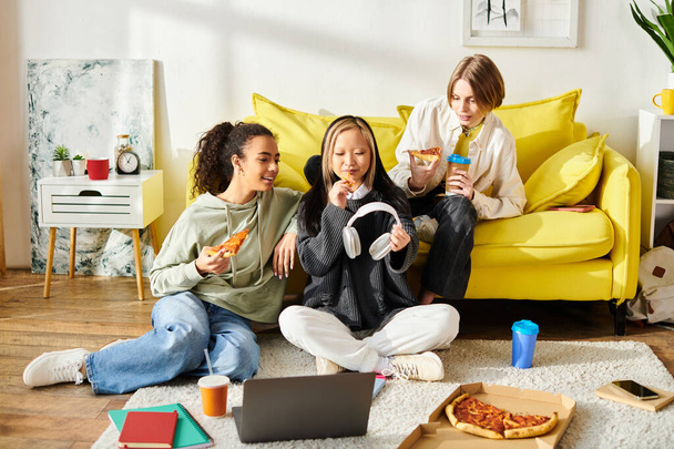 Trois adolescentes diverses assises sur le sol ensemble, dégustant un repas de pizza. - Photo, image