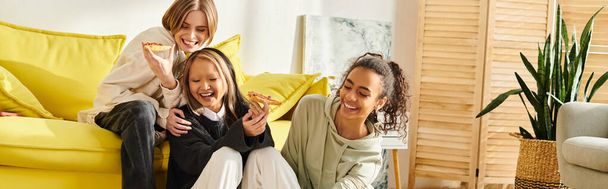 女性と2人の異人種間の十代の少女が活気に満ちた黄色のソファーに座って,互いに楽しんでいます. - 写真・画像