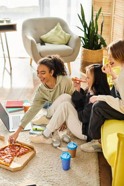 Vielfältige Gruppe Teenager-Mädchen, die an einem Tisch sitzen und zu Hause gemeinsam eine Pizza genießen. - Foto, Bild