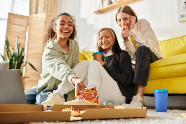 Monipuolinen ryhmä teinitytöt nauttivat rento ajanviettopaikka, istuu lattialla, ja nauttivat pizza viipaleita yhdessä. - Valokuva, kuva