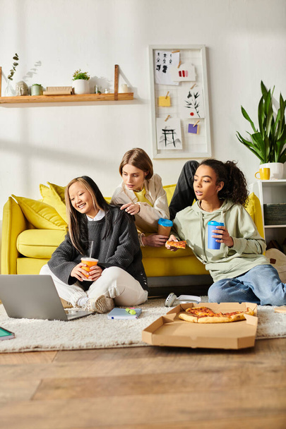 Gruppe Teenager-Mädchen verschiedener Rassen teilen Lachen und Pizza, während sie zusammen auf einer gemütlichen Couch sitzen. - Foto, Bild