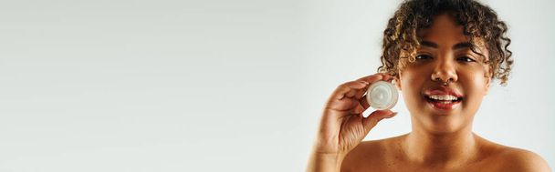 Очаровательная афроамериканка, демонстрирующая банку крема. - Фото, изображение