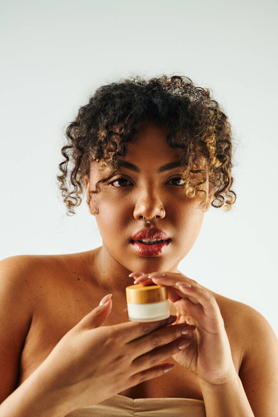 Femme afro-américaine exsudant grâce, tenant une crème, sur fond vibrant. - Photo, image