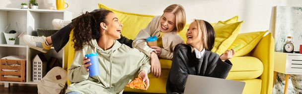 Eine bunte Gruppe Teenager-Mädchen unterschiedlicher Rassen sitzt zusammen auf einer leuchtend gelben Couch, lächelt und plaudert und präsentiert die Schönheit der Freundschaft.. - Foto, Bild
