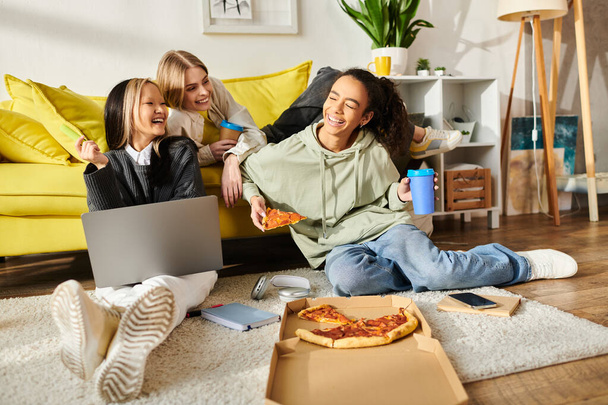 Bir grup genç kız yerde birlikte oturuyor, rahat bir evde pizza dilimlerinin tadını çıkarıyorlar.. - Fotoğraf, Görsel
