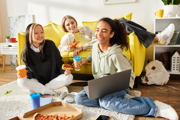 Tinédzser lányok sokszínű csoportja ül a földön, boldogan esznek együtt pizzát.. - Fotó, kép