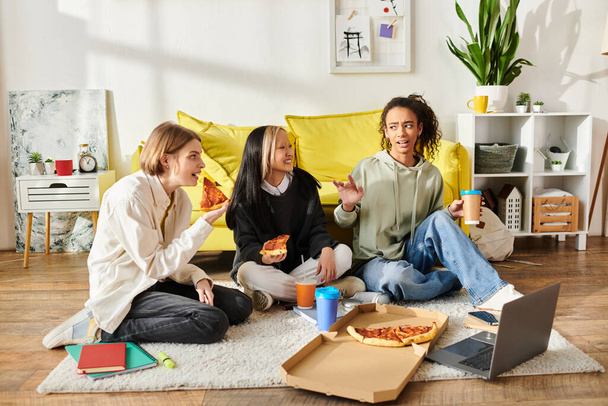 Un variegato gruppo di ragazze adolescenti si siede sul pavimento, condividendo gioiosamente la pizza insieme in un ambiente accogliente a casa. - Foto, immagini