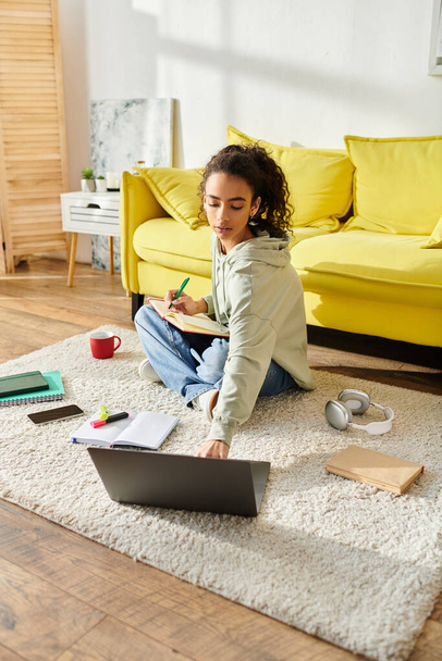 Una adolescente sentada en el suelo, absorta en el aprendizaje electrónico en su portátil. - Foto, Imagen