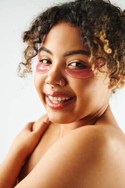 Cheerful African American woman showcasing eye patches on a vibrant backdrop. - Photo, Image