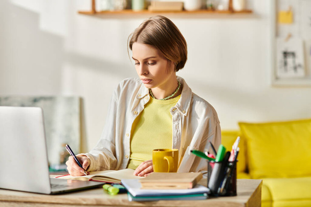 Een tienermeisje zit aan een tafel, studeert met een laptop en nipt koffie. - Foto, afbeelding