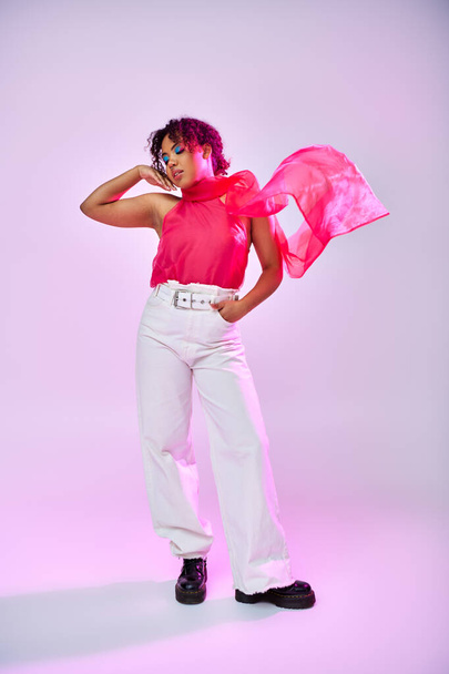 Mujer afroamericana posando en camisa rosa y pantalones blancos sobre un vibrante telón de fondo. - Foto, imagen