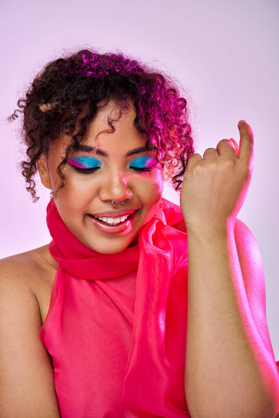 Una bella donna afroamericana che colpisce una posa in una sciarpa rosa e ombretto blu. - Foto, immagini