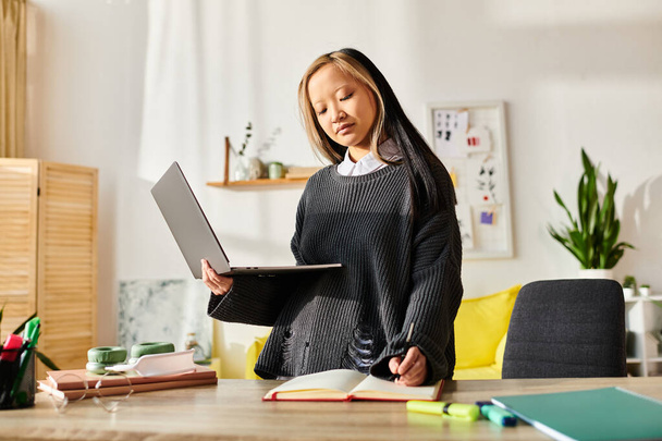 Una giovane ragazza asiatica impegnata nell'e-learning a casa, in piedi di fronte a un computer portatile. - Foto, immagini