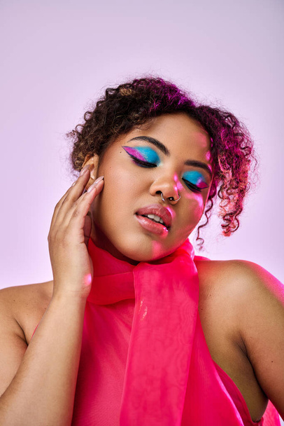 African American woman wearing a pink dress and bold makeup strikes a dynamic pose against a vibrant backdrop. - Photo, Image