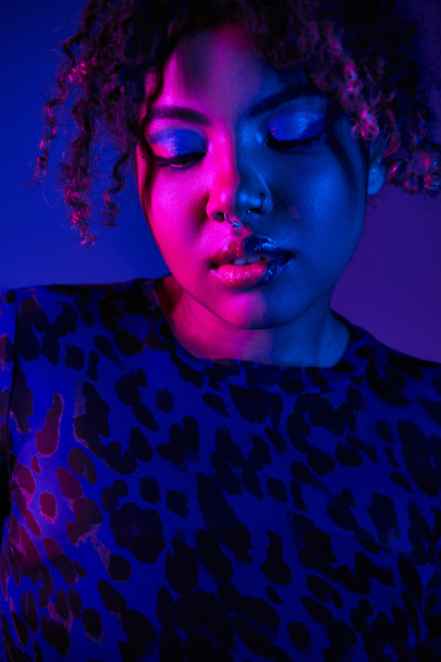 Une femme afro-américaine frappante aux yeux bleus portant une chemise imprimée léopard pose sur un fond vibrant. - Photo, image