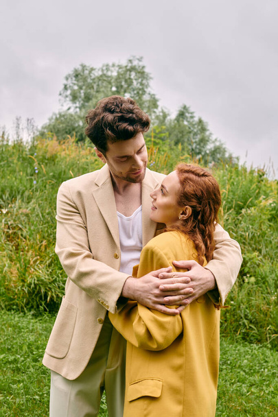Un hombre y una mujer comparten un tierno abrazo en un exuberante campo verde, rodeado de la belleza de la naturaleza. - Foto, Imagen