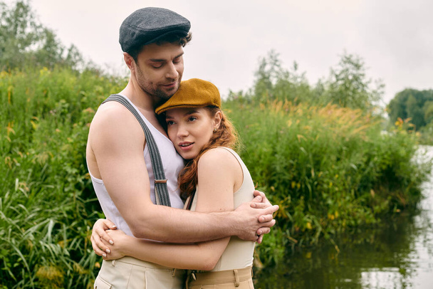 Ein Mann und eine Frau umarmen sich innig vor einem ruhigen Gewässer in einem grünen Park. - Foto, Bild