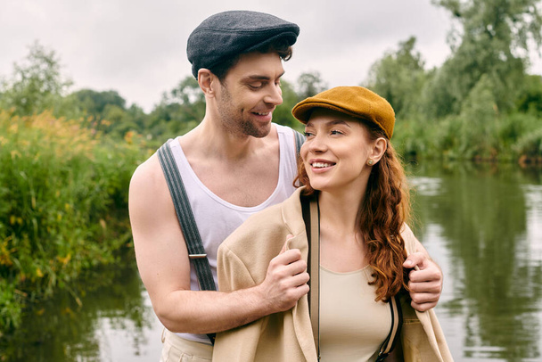 Un hombre y una mujer de pie junto al río, disfrutando de una cita romántica en un hermoso entorno de parque verde. - Foto, imagen