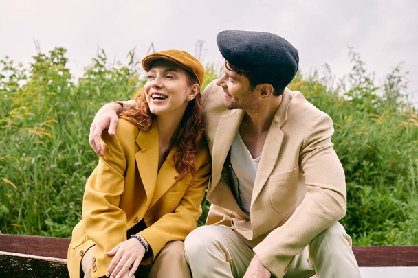 Um homem e uma mulher sentam-se pacificamente em um banco em um parque verde, desfrutando de um encontro romântico em meio a um ambiente natural.. - Foto, Imagem