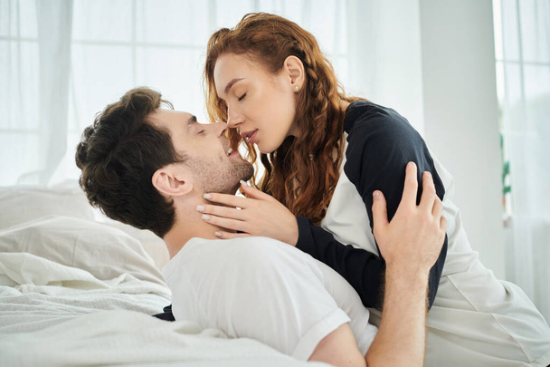 Чоловік ніжно цілує жінку на щоці, висловлюючи любов і близькість в затишній обстановці спальні. - Фото, зображення