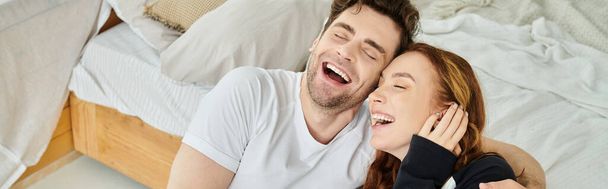 Egy férfi és egy nő feküdt az ágyon, megosztva a tiszta öröm pillanatát, ahogy együtt nevetnek.. - Fotó, kép