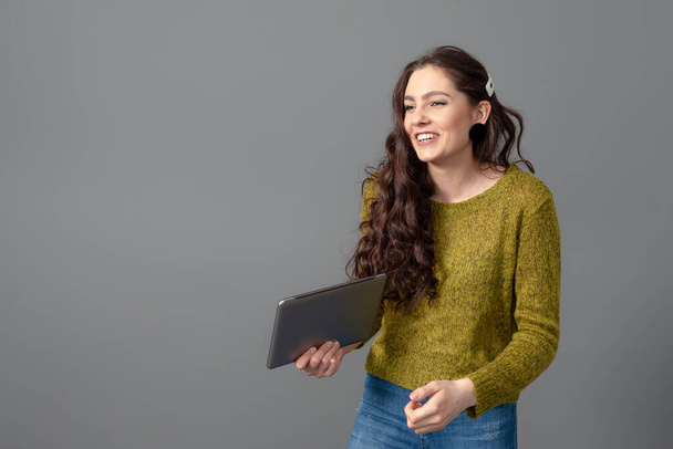 tiener vrouw met lang golvend haar en tablet in handen, geïsoleerd op een grijze achtergrond - Foto, afbeelding