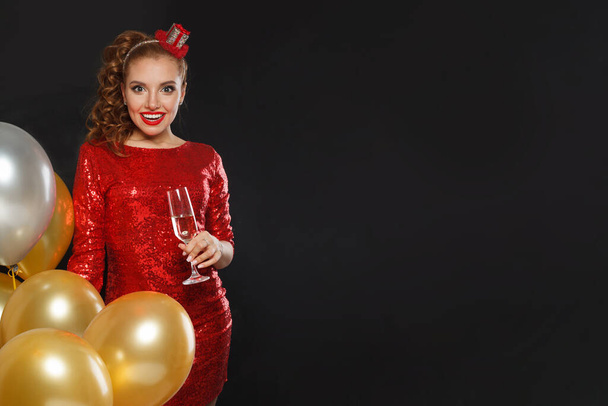 Excitada mulher surpresa feliz com maquiagem e penteado vestindo vermelho brilhante lantejoulas vestido segurando balões de festa, surpresa, presentes e Natal feriado celebração fundo - Foto, Imagem