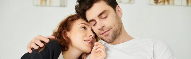 Een man en een vrouw die dichtbij elkaar staan en een moment van intimiteit en verbondenheid delen in een slaapkameromgeving. - Foto, afbeelding