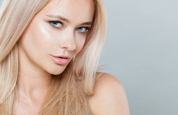 Charmante vrouw gezicht close-up. Blond model met frisse heldere huid en gezond zijdezacht haar op witte achtergrond  - Foto, afbeelding