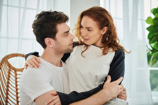 Ένας άντρας και μια γυναίκα αγκαλιάζονται τρυφερά, εκφράζοντας αγάπη και οικειότητα σε ένα γαλήνιο περιβάλλον κρεβατοκάμαρας.. - Φωτογραφία, εικόνα