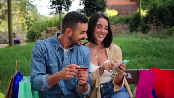 Young caucasian couple watching a smartphone bet application. Two friends using a cellphone to browse on internet. Real people shopping online with a mobile phone app. Man and woman on social media - Footage, Video