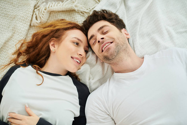 Un hombre y una mujer se relajan juntos en una cama en un acogedor dormitorio, disfrutando de la compañía de los demás en un momento de paz. - Foto, Imagen