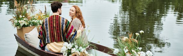 A couple in boho attire peacefully row a boat adorned with flowers in a lush green park. - Photo, Image