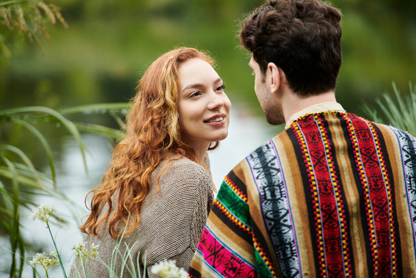 Egy elegáns férfi és nő bohém öltözékben szorosan együtt állnak egy buja zöld parkban, szeretetet és kapcsolatot árasztva.. - Fotó, kép