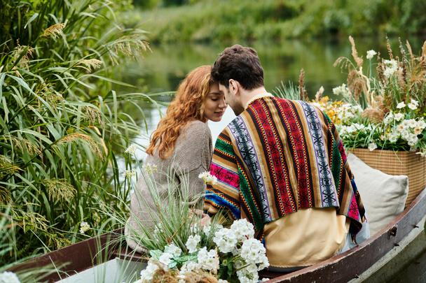 A man and woman dressed in boho style clothes drift in a boat adorned with flowers through a lush green park. - Photo, Image