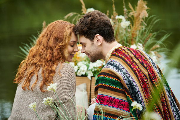 Een man en een vrouw, gekleed in boho stijl kleding, zitten samen in een weelderig groen park, stralen romantische en zorgeloze vibes. - Foto, afbeelding