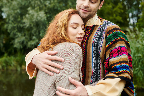 Un uomo e una donna in abito boho abbracciano teneramente in un parco verde, trasudando amore e serenità nel loro momento romantico.. - Foto, immagini