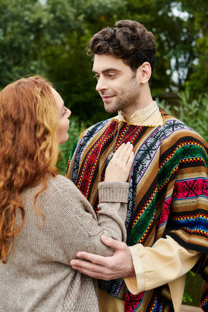 Een man en een vrouw in boho kleding staan samen in een groen park, omgeven door serene schoonheid. - Foto, afbeelding