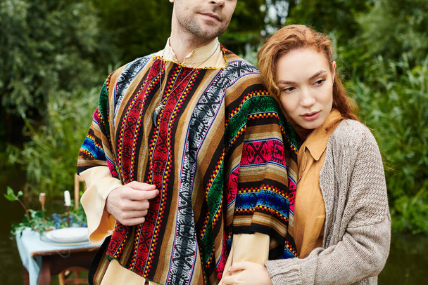 Un homme et une femme dans des vêtements de style boho se tiennent étroitement ensemble dans un cadre de parc verdoyant, respirant l'amour et la connexion. - Photo, image