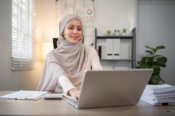 Empresaria musulmana asiática en pañuelo de cabeza de hiyab trabajando con documento de papel en la oficina moderna. diversidad y concepto de oficina. - Foto, imagen